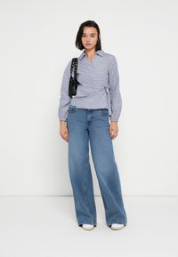 Μπλε πουκάμισο με καρό σχέδιο και μακριά μανίκια, συνδυασμένο με μπλε τζιν παντελόνι με φαρδιά μπάλα και λευκά αθλητικά παπούτσια. Μαύρη τσάντα με λουρί διακοσμημένο με καρφιά.