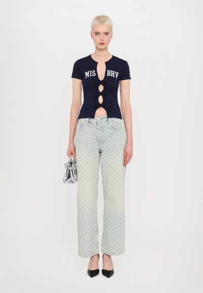 Navy short-sleeve top with cut-out design and bow accents, paired with light blue patterned jeans and black pointed-toe heels. Clear handbag.