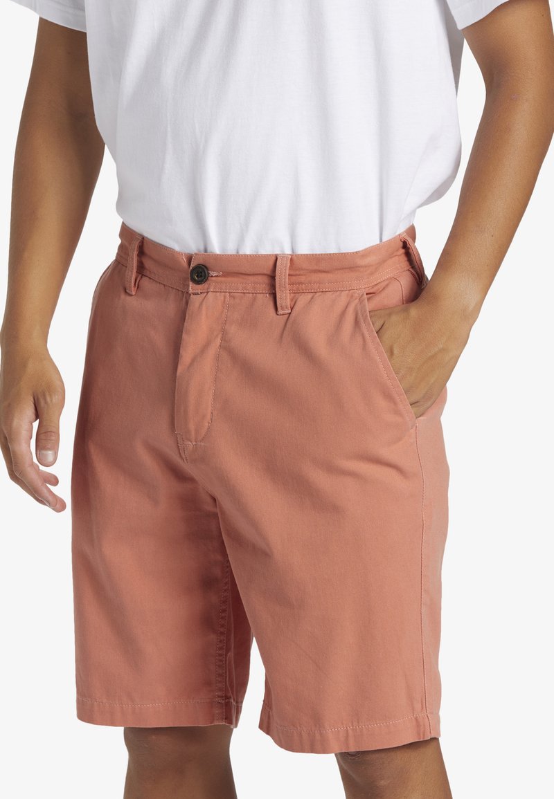 Shorts en tissu doux de couleur corail, avec une fermeture à bouton, des passants de ceinture et des poches latérales. Longueur standard et coupe droite.