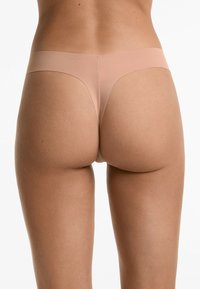 Huidskleurige thongonderbroek van gladde stof, met een naadloos ontwerp en minimale bedekking, voorzien van een zachte elastische tailleband.
