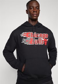 Fekete kapucnis pulóver, amelyen piros betűkkel szerepel a "Chicago Bulls" felirat lángmintákkal, puha anyagból készült, kenguru zsebbel és állítható kapucnival.