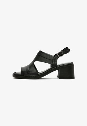 Sandales noires en cuir à talons avec design découpé, bride adjustable à la cheville et talon en bloc texturé. Présente une finition lisse et des détails de couture.