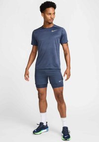 Camisa deportiva Nike de color navy con textura a rayas y logo, combinada con pantalones cortos a juego, calcetines blancos y zapatillas azul con acentos verdes.