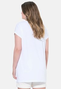 Vit t-shirt med kort ärm och avslappnad passform, gjord av mjukt bomullsmaterial och rund halsringning. Bakifrån visas detaljer om axlar och hår.