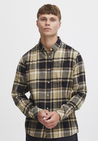 Beige, musta ja halli ruuduline pikkade varrukatega särk, millel on nööpidega eesmine osa, rinnatasku ja pehme, tekstuuriga kangas.