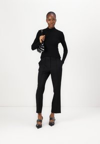 Black fitted turtleneck, tailored black trousers, and black heeled shoes with buckle details. Minimalist design against a white background.