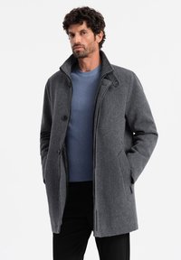 Abrigo de mezcla de lana gris con un alto cuello, cierres de botón, bolsillos laterales y un interior texturizado, usado sobre un suéter azul de canalé.