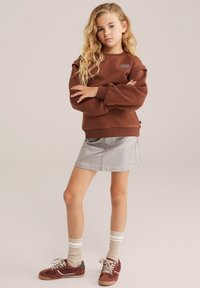 Rjava sweatshirt z nabranimi rokavi, v kombinaciji s srebrno denim krilom. Obut z burgundskimi supergami in svetlo črtastimi nogavicami.