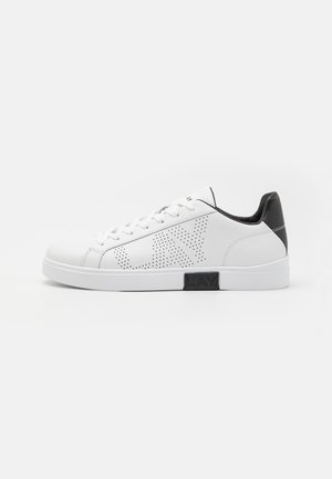 Hvit lær sneakers med perforert design, svart hæl og midtsåle. Har rund tå og seks hull for snøring.