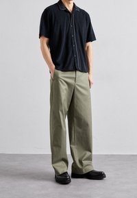 Musta, lyhythihainen paita, jossa on kontrastinen kaulus, yhdistettynä leveisiin, vaaleanoliivivihreisiin housuihin ja mustiin nauhakenkiin.