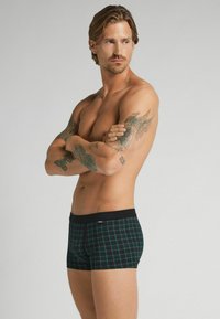 Svart och grön rutiga boxershorts med svart midjeband; har en mjuk tygkänsla och en åtsittande passform. Inga synliga logotyper eller mönster.