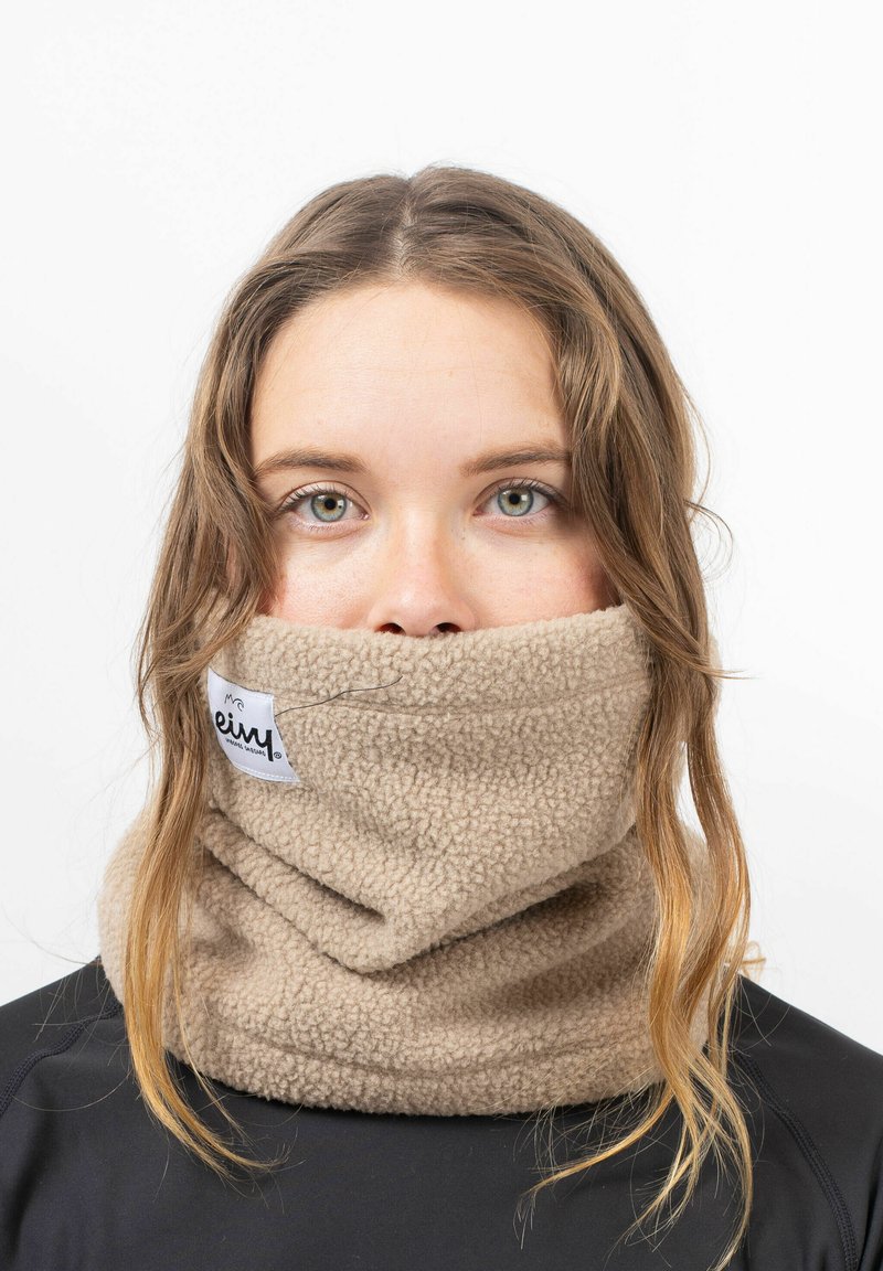 Gaiter en polaire beige avec une texture douce, portant une étiquette avec le nom de la marque. Porté autour du cou, couvrant une partie du bas du visage.