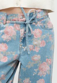 Jean en denim bleu clair avec un motif floral rose et une fine ceinture en denim nouée en un nœud à la taille.