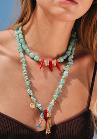Deux colliers superposés ornés de perles turquoise, d'accents rouges, de matériel doré et de charms décoratifs, y compris un poisson et un gland.