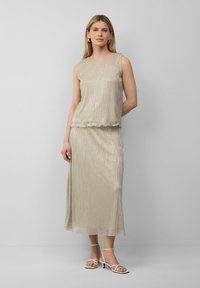 Lichtgouden twee-delige set met een mouwloze top en een enkellange rok. Bevat een subtiele glans en een scalloped zoom. Wit met straps hiel.