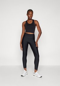 Top corto atlético negro combinado con mallas negras de talle alto. La modelo lleva zapatillas deportivas blancas. Textura suave con un diseño ajustado.