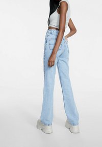 Jeans de cintura alta azul claro con corte de pierna ancha, que cuentan con bolsillos traseros y un dobladillo sin terminar, combinados con una blusa sin mangas gris.