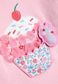 Ružová látka s vyšitým cupcačkom s čerešňou, obklopená ružovými kvetinovými aplikáciami a malou šedou nášivkou slona s akcentmi.