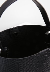 Sort håndtaske med en textured slangeskinds-mønster. Indersiden er foret med glat stof og har en trykknaplukning samt robuste håndtag.