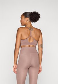 Sutiã desportivo em mauve, com um design de costas nadador e um recorte em forma de chave. O material parece elástico e suave, combinado com leggings de cintura alta.