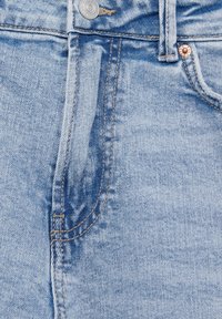 Des jeans en denim bleu clair présentent des accessoires en cuivre et en argent contrastants, des détails de couture visibles et une texture lisse.