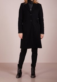 Zwarte wollen jas met een op maat gemaakt ontwerp, enkel-breasted voorkant, notch revers en zijzakken. Gecombineerd met aansluitende zwarte pantalon en zwarte cowboylaarzen.