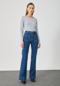 Maglietta a maniche lunghe grigia chiara abbinata a jeans a vita alta blu scuro a campana, con tasche anteriori e una cintura nera con fibbia argentata.