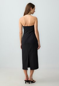 Abito midi nero a coste con design senza spalline, zip sul retro e uno spacco centrale all'orlo. Presenta una texture liscia e una silhouette aderente.