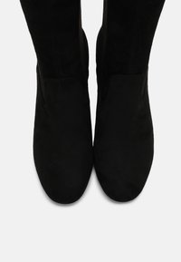 Botas cortas de ante negro con punta redondeada, que presentan una textura suave y un diseño minimalista, sin ningún hardware o adornos visibles.