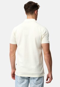 Polo-shirt i off-white med krave og korte ærmer, lavet af et bl�ødt, tekstureret stof og med en let forlængelse ved kanten.