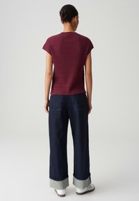 Burgundy, textured short-sleeve top paired with wide-leg denim pants featuring rolled cuffs and back pockets, worn with white sneakers.