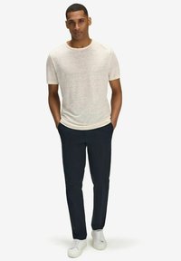 Lys beige kortærmet t-shirt parret med mørkeblå bukser og hvide sneakers. T-shirten har en subtil tekstur og en rund halsudskæring.