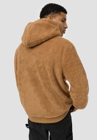 Brown fleece hoodie with a textured surface, featuring a drawstring hood and ribbed hem. The fabric appears soft and thick.