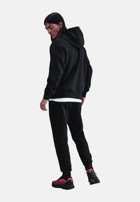 Zwarte hoodie en bijpassende joggers van gestructureerde stof, gecombineerd met zwart-rode sportschoenen met een opvallend zoolontwerp.