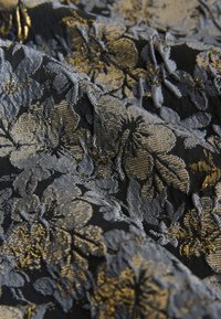 Textil fekete alapon, ezüst és arany szálakkal szőtt virágmintával. Simább tapintású, részletesen kidolgozott virágmintákkal.