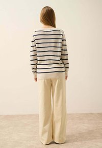 Kremowy sweter w granatowe paski, luźny krój i ściągacze, zestawiony z szerokimi beżowymi spodniami z kordurowej tkaniny, widok z tyłu.