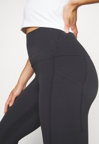 Leggings neri con vita alta, dotati di dettagli di cucitura, texture liscia e tasca laterale, progettati per un uso attivo.