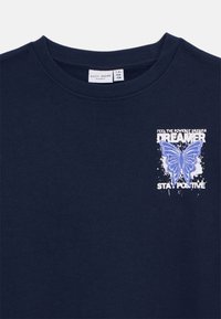 T-shirt en coton bleu marine avec un col ras du cou côtelé, arborant un graphisme de papillon blanc et bleu clair ainsi que le texte "DREAMER STAY POSITIVE."