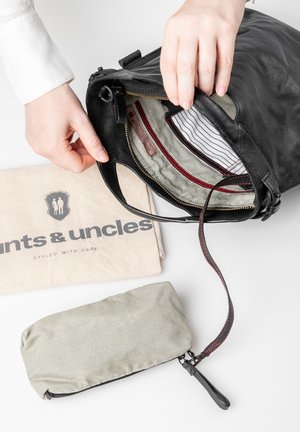 Schwarze Lederhandtasche mit gestreiftem Stofffutter, roten Akzenten, Reißverschluss und abnehmbarem Umhängeriemen. Enthält ein beiges Stofftäschchen und ein graues Reißverschlusstäschchen.