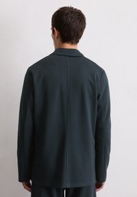 Donkergroene, textuurjasje met een kraag, met een rechte snit en minimale stikdetails op de achterkant.