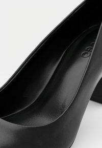 Shoe nera in pelle con tacco alto, superficie liscia, punta arrotondata e tacco largo. Nessun marchio o decorazione visibile.