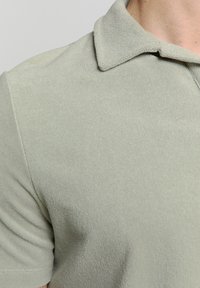 Lichtgroene polo met een textuurstof, voorzien van een klassieke kraag en korte mouwen, die een soepele maar comfortabele uitstraling benadrukt.