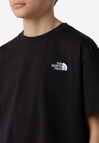 Black cotton t-shirt featuring a round neckline and short sleeves. Includes a white embroidered logo on the chest, simple and clean design.