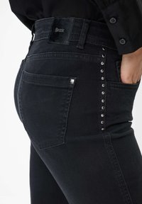 Jeans neri in denim con una vestibilità slim, caratterizzati da una texture liscia, borchie argentate lungo il lato e un'etichetta in pelle nera con il marchio sul retro.
