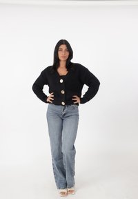 Cárdigan negro de punto con escote en V y cuatro grandes botones dorados, combinado con jeans de tiro alto en azul claro y zapatos de plataforma nude.