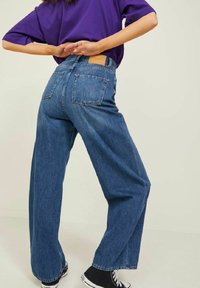 Jeans in denim blu a gamba larga con vita alta, tasche posteriori e tessuto testurizzato. Abbinati a scarpe da ginnastica in tela nera.