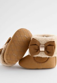 Barna velúr kisgyermek csizmák műszőrme béléssel, lapos gumitalppal és nagy textil masnival a hátsó részen; mintás tapadós talppal ellátott borítás.