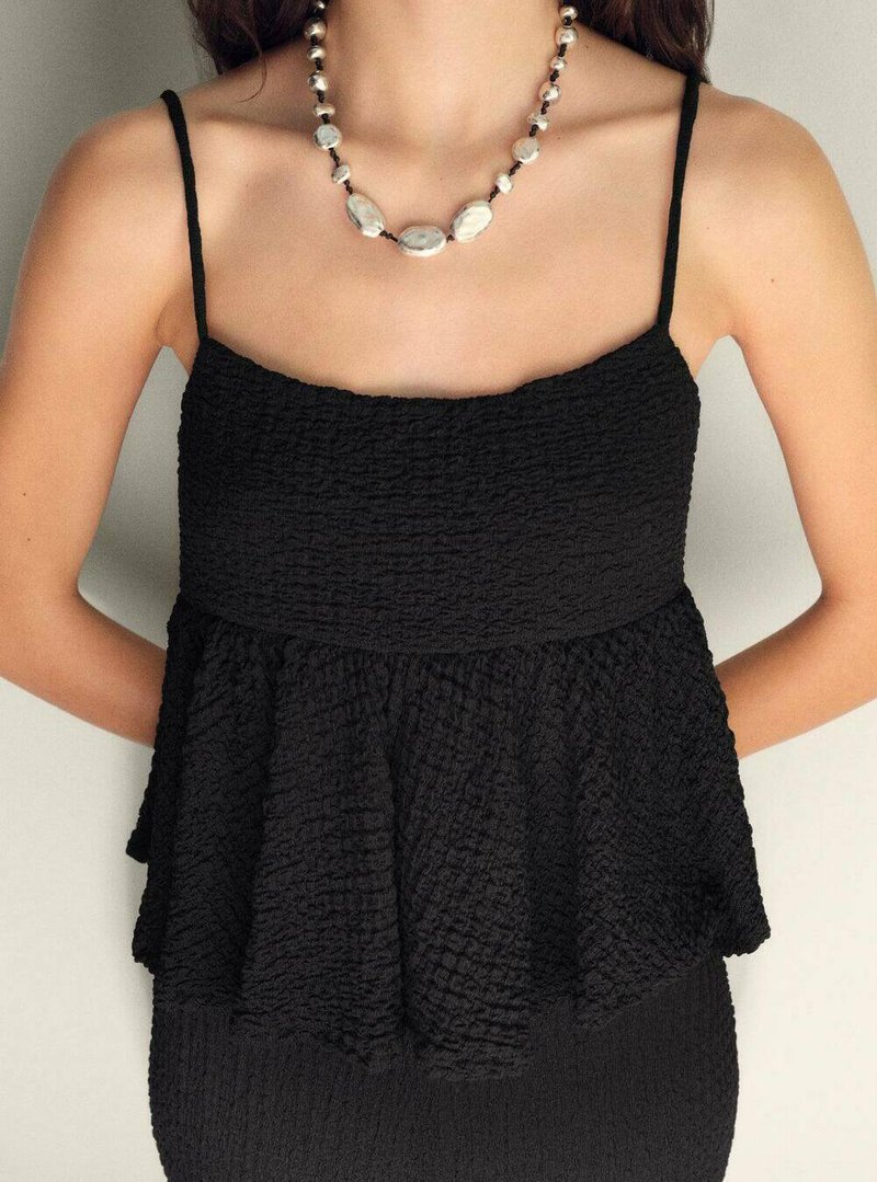 Top peplum negru cu bretele subțiri, realizat dintr-un material texturat. Include un design cu model și este asortat cu un colier distinctiv din mărgele.