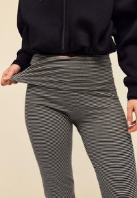 Schwarz-weiß gestreifte Leggings aus weichem Stoff, mit hohem Bund und enger Passform, getragen zu einem schwarzen Zip-up-Hoodie.