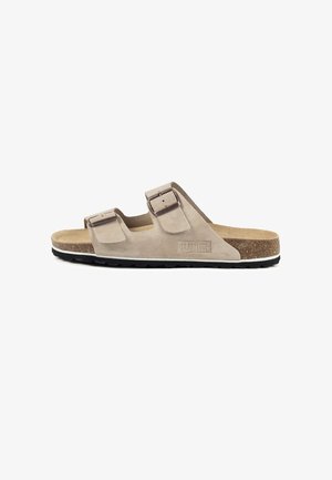Sandalia tipo slide de ante beige con dos correas ajustables, plantilla de corcho y suela exterior de goma negra. Presenta el logo de la marca en un lateral.